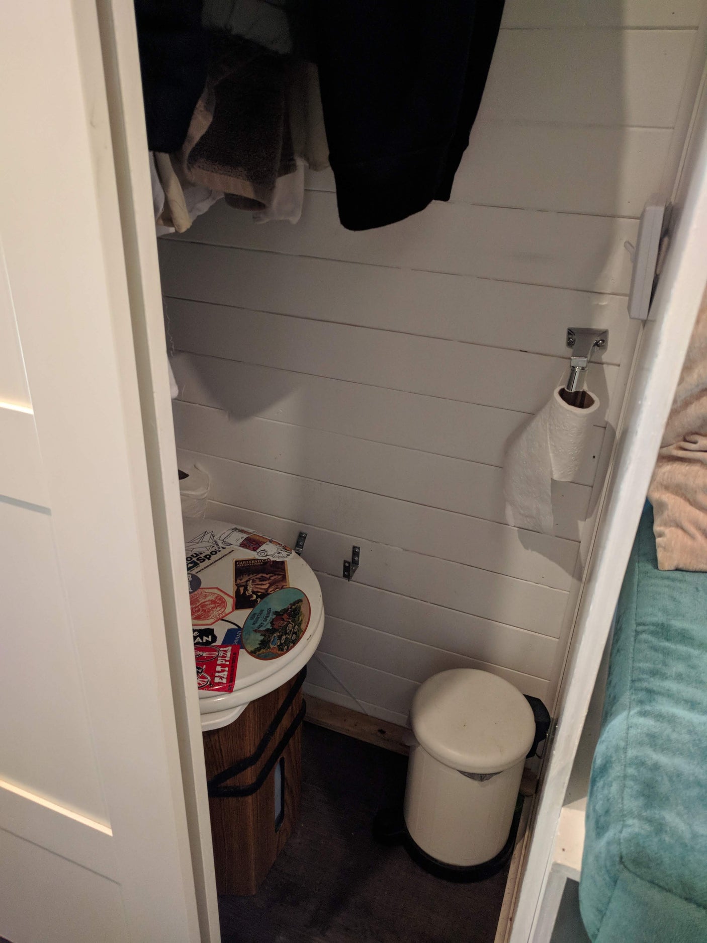 Inside a compact RV rental, a toilet with travel stickers, toilet paper holder, and small trash can are visible.