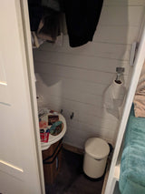 Inside a compact RV rental, a toilet with travel stickers, toilet paper holder, and small trash can are visible.