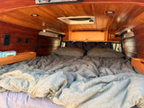 Cozy wood-paneled RV rental interior features a large bed with gray bedding, built-in outlets, and storage.
