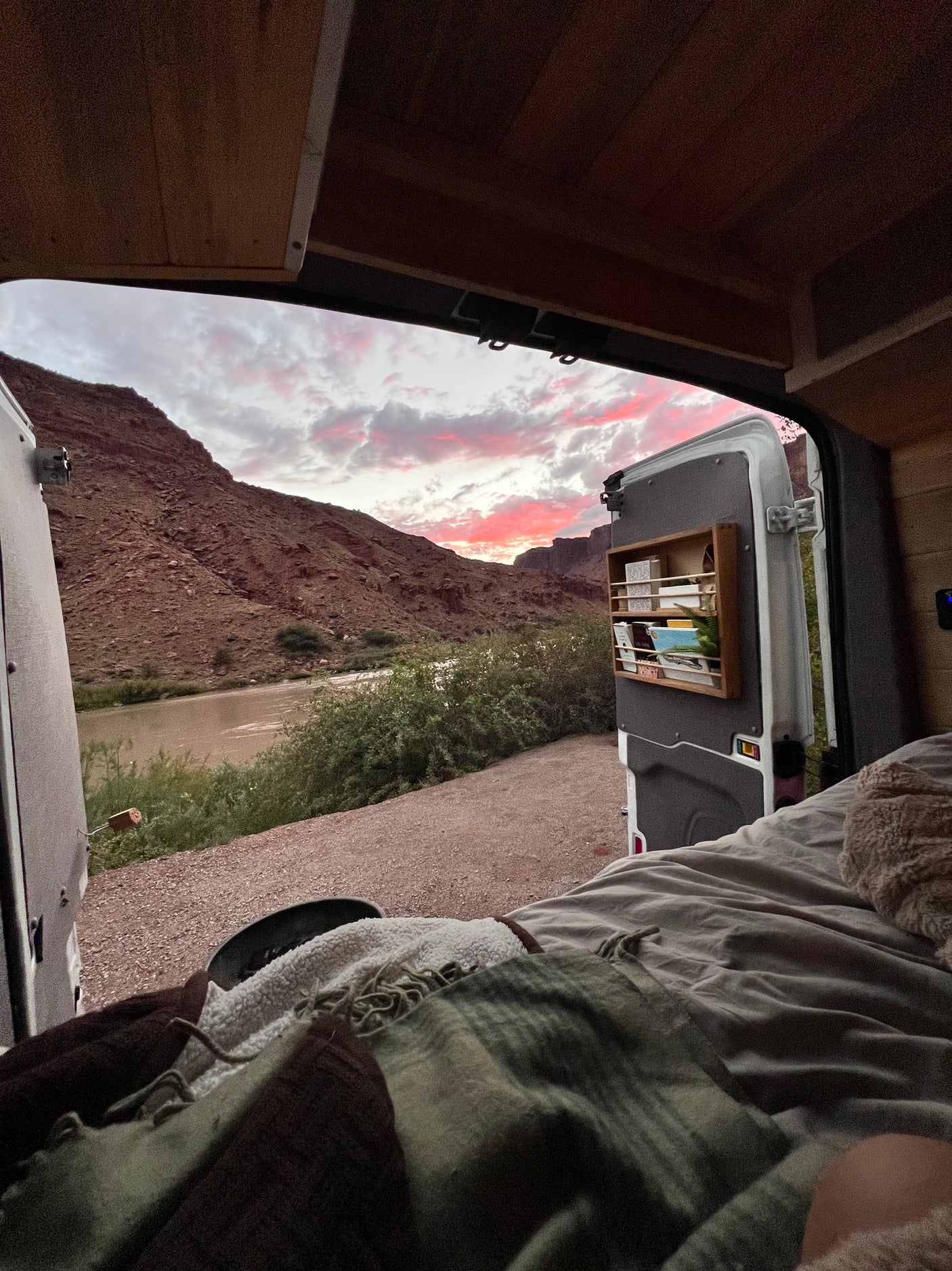 RV rental comfort: stunning sunset view over river and mountains from a cozy van bed. Perfect van life escape!