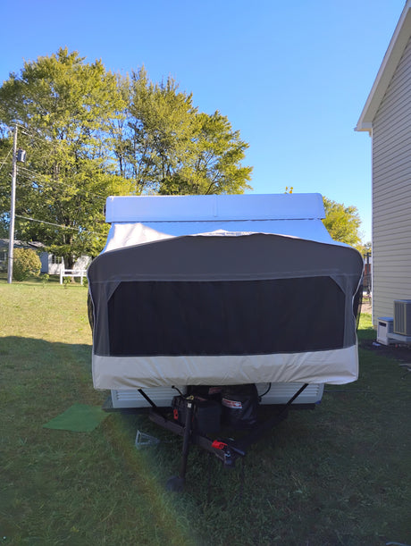 Front view of a covered pop-up camper, ready for an rv rental adventure, parked in a sunny yard.