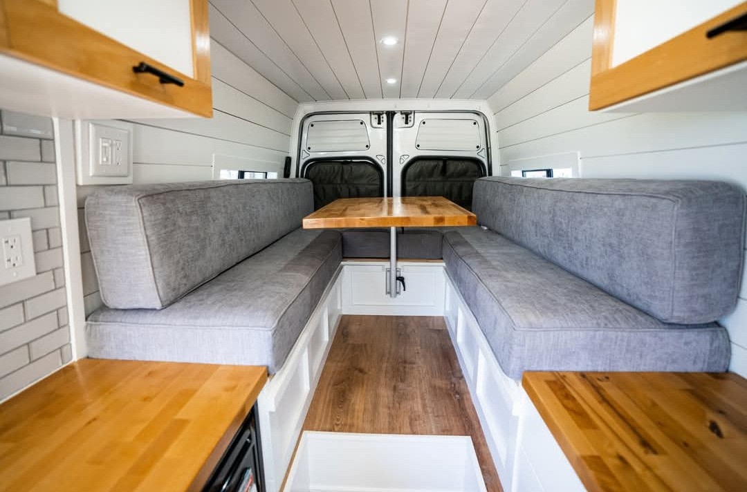 This RV rental features a clean, cozy dining area with two long gray-cushioned benches facing a wooden table. — photo 6