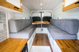 This RV rental features a clean, cozy dining area with two long gray-cushioned benches facing a wooden table.