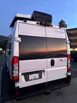 White Winnebago Solis camper van for **rv rental**, its rear windows reflecting a stunning sunset over water.