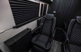 Inside a high-end rv rental, showing two black leather captain chairs with diamond stitching and a side console with cup holder.