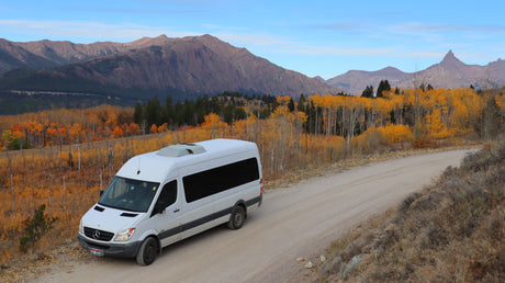 Fall adventure with an RV rental: a white Sprinter van on a scenic dirt road, framed by mountains and brilliant autumn aspens.