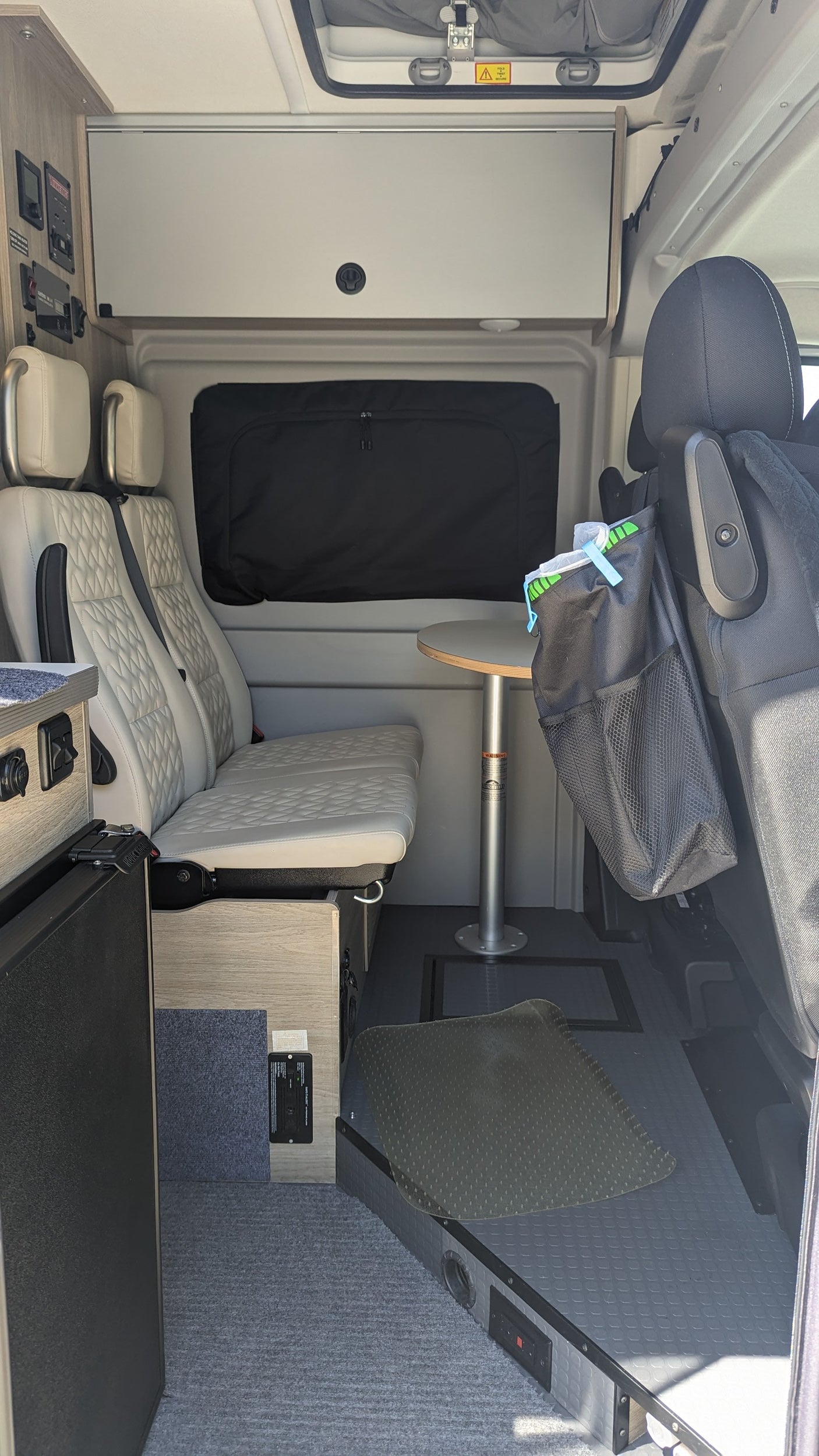 RV rental: Inside a modern camper van with comfortable quilted seating, a round table, overhead storage, and varied floor types.