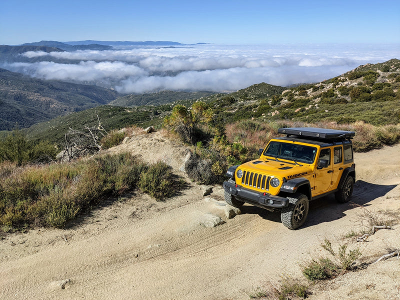  showcasing expansive mountain views through large arched windows. Ideal for nature lovers.|Bright yellow Jeep Rubicon on a snowy trail beside a reflective lake with mountains.|Yellow Jeep Rubicon with rooftop tent on a mountain trail overlooking clouds. Consider an RV rental for views like this!|Bright yellow Jeep with deployed roof-top tent — photo 8