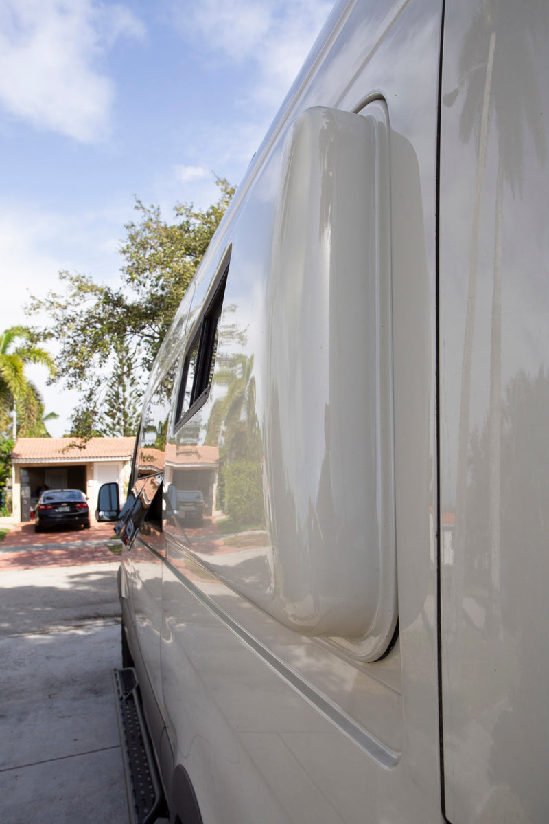 This RV rental's shiny white side with a window and pop-out enclosure reflects a house & trees under a blue sky. — photo 10