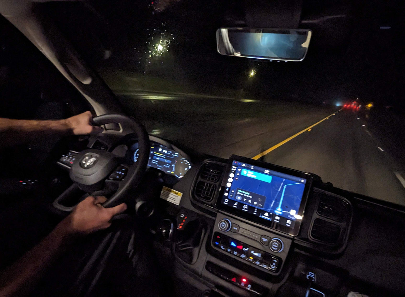 Nighttime **rv rental** drive: hands on the steering wheel, navigation screen lit, guiding the way on a dark road.