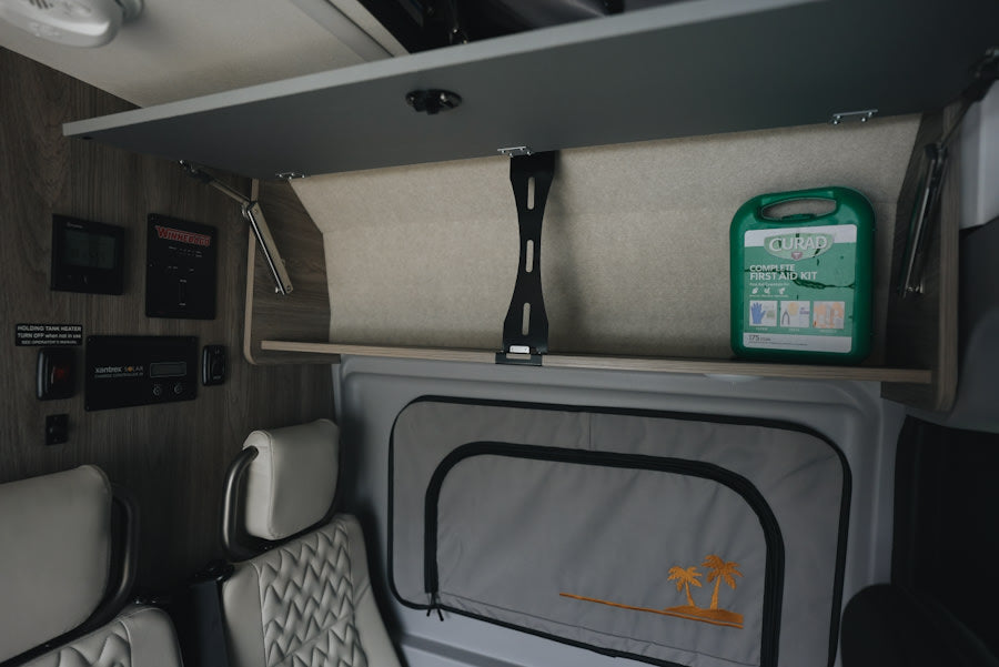 An RV rental's well-equipped interior: a first aid kit in the overhead storage, control panels, and upholstered seating.