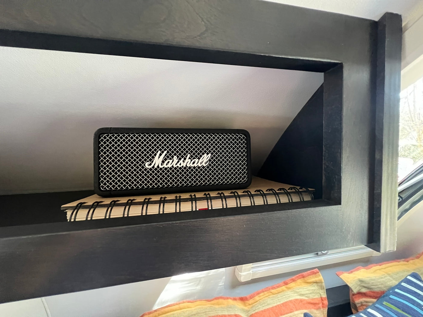 A Marshall speaker and notebook neatly placed in an RV rental's dark built-in cubby, ideal for road trip tunes and notes.