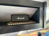 A Marshall speaker and notebook neatly placed in an RV rental's dark built-in cubby, ideal for road trip tunes and notes.