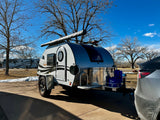 Ready for an outdoor adventure! A "Boondock Lite" teardrop RV rental is hitched to a vehicle on a sunny day.