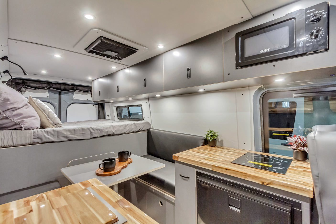 RV rental interior: modern camper van featuring a bed, kitchen with microwave & cooktop, and dining area.