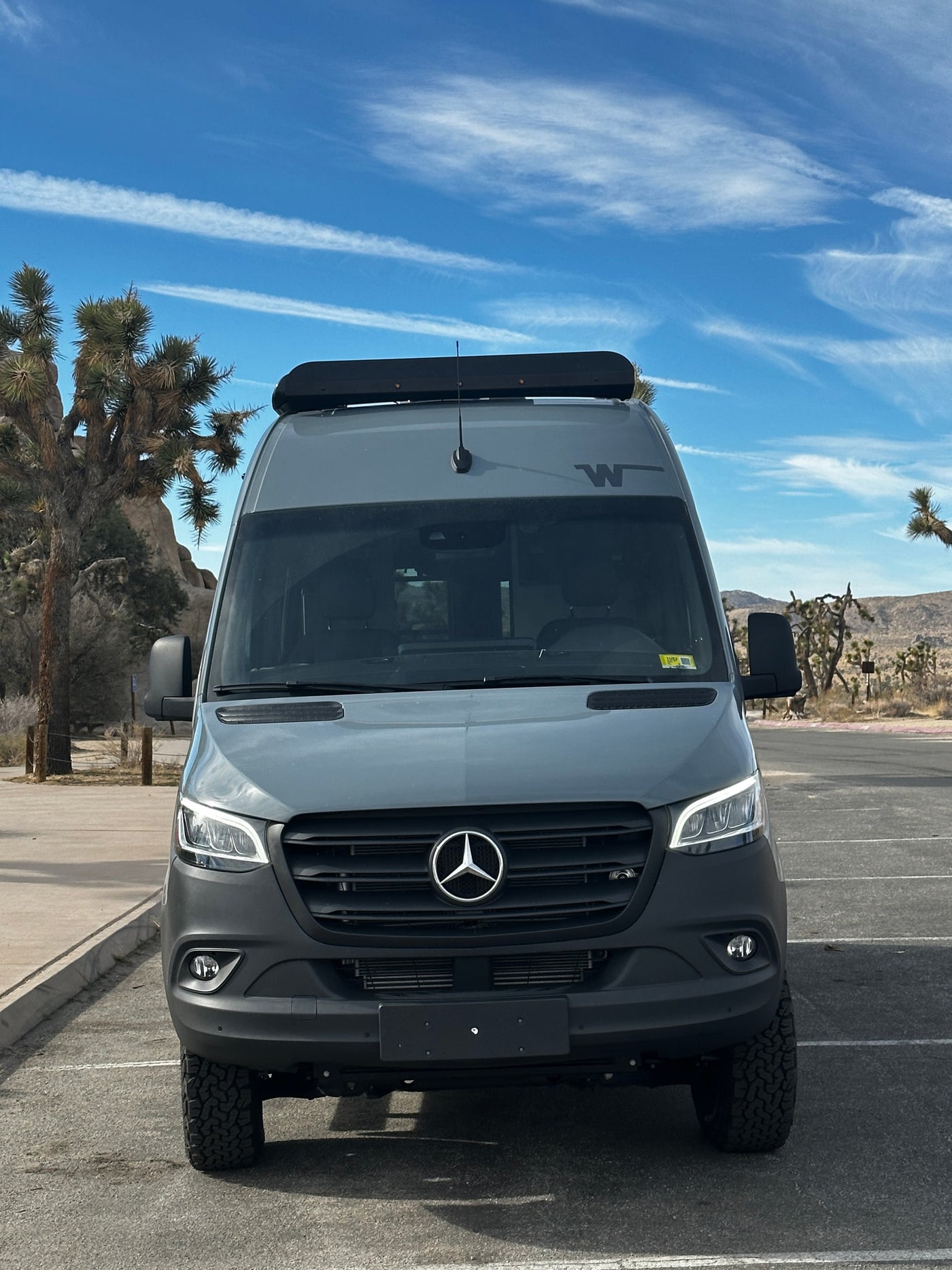Front view of a grey Mercedes Sprinter RV rental, parked in a desert landscape with Joshua trees under a blue sky. — photo 4