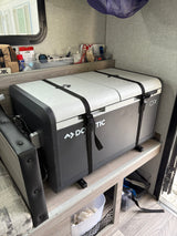 Dometic CFX portable fridge securely strapped in an RV rental, with organized shelves above for camping essentials. Perfect for travel.