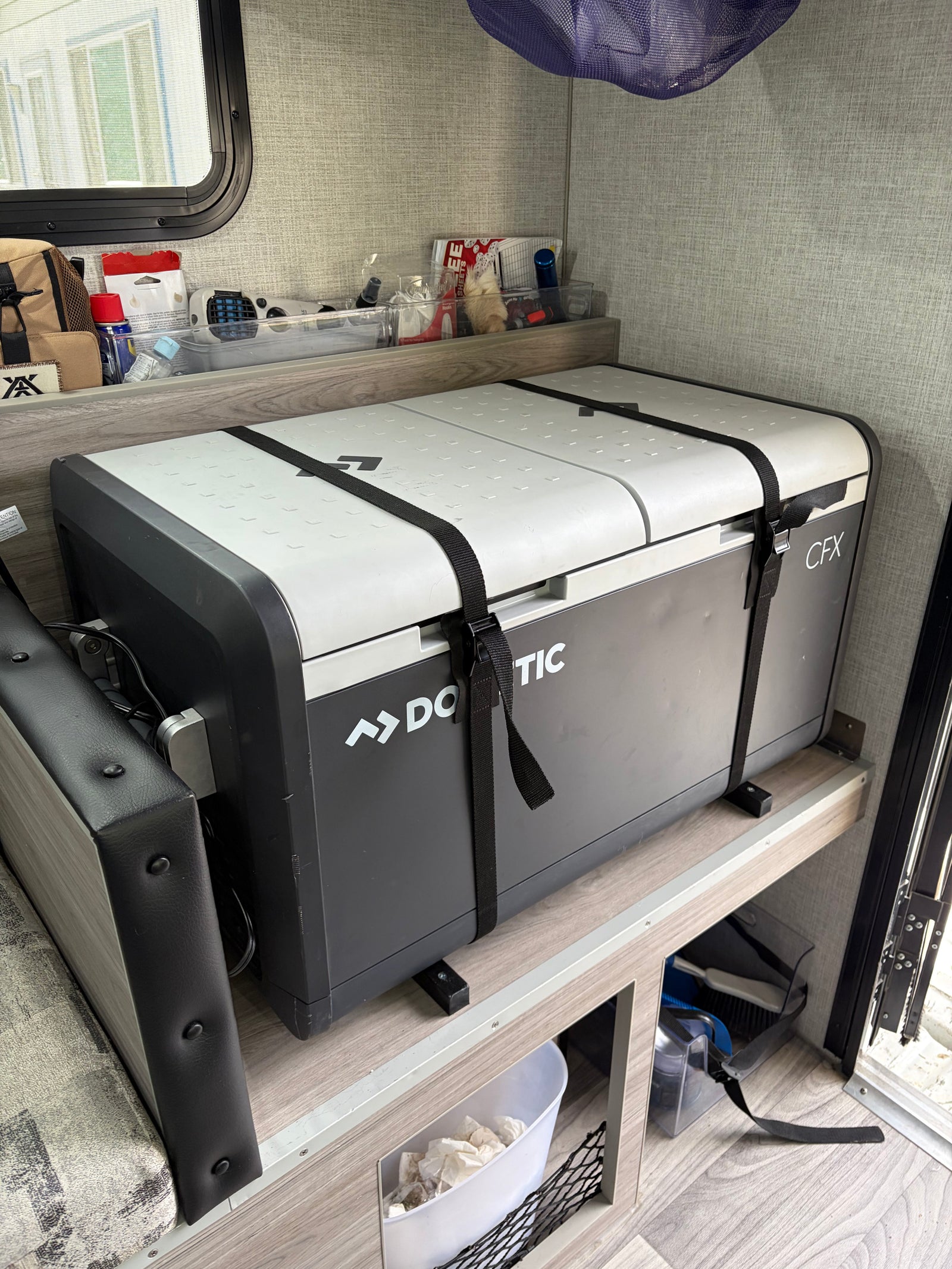 Dometic CFX portable fridge securely strapped in an RV rental, with organized shelves above for camping essentials. Perfect for travel.