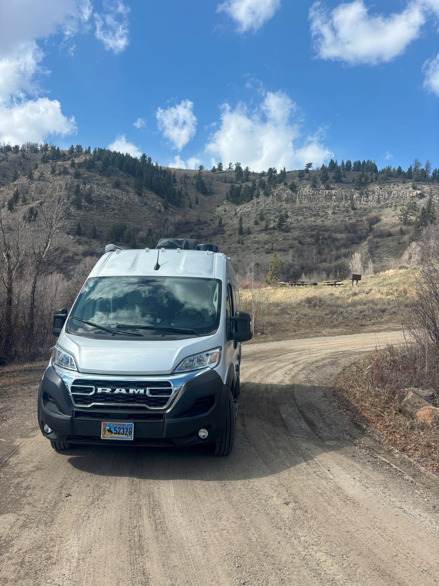 White Ram RV rental van on a dirt road in Wyoming, with mountains and a picnic area under a blue sky.