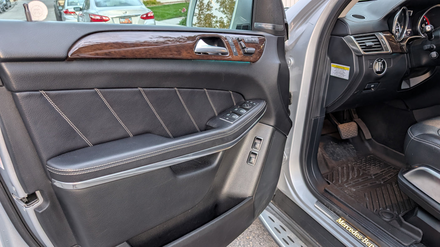 Luxury car interior: driver's door with glossy wood trim, stitched black leather, & controls. A refined auto experience, distinct from an rv rental.