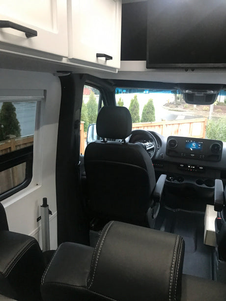 Inside this RV rental: driver's area, dashboard, passenger seating, white overhead cabinets, and an entertainment screen.