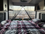 Relaxing in an RV rental, looking out at a stunning marina. Cozy plaid bed, boats, and docks create a serene waterfront view.