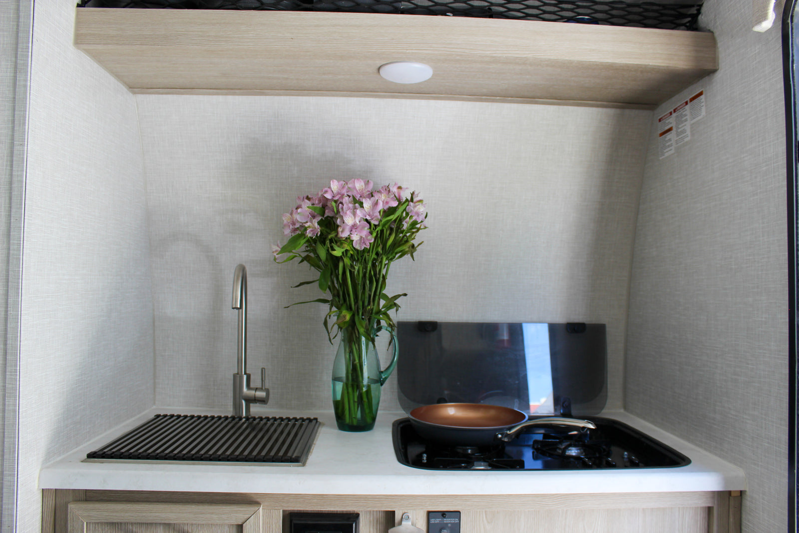 Compact RV rental kitchen featuring a sink, stove, and fresh flowers, ready for your travel adventures.