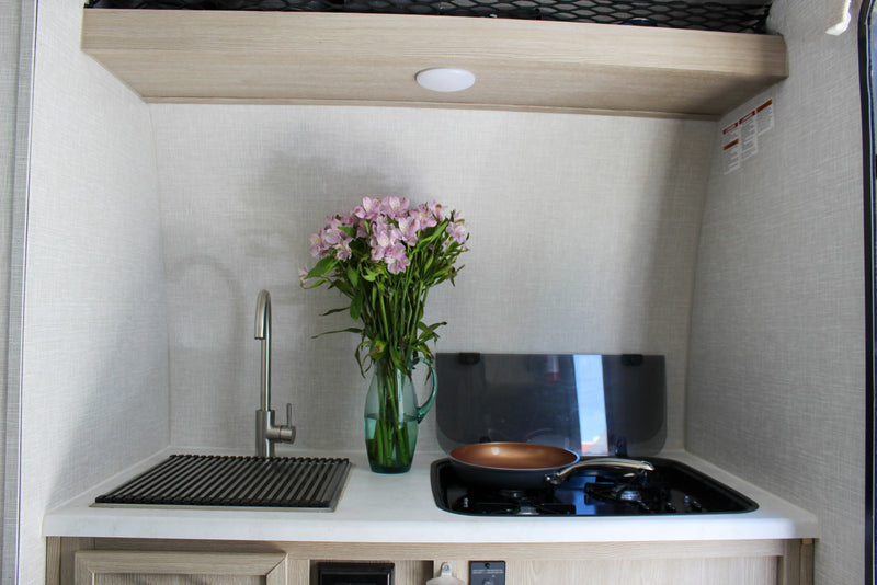 Compact RV rental kitchen featuring a sink, stove, and fresh flowers, ready for your travel adventures. — photo 8
