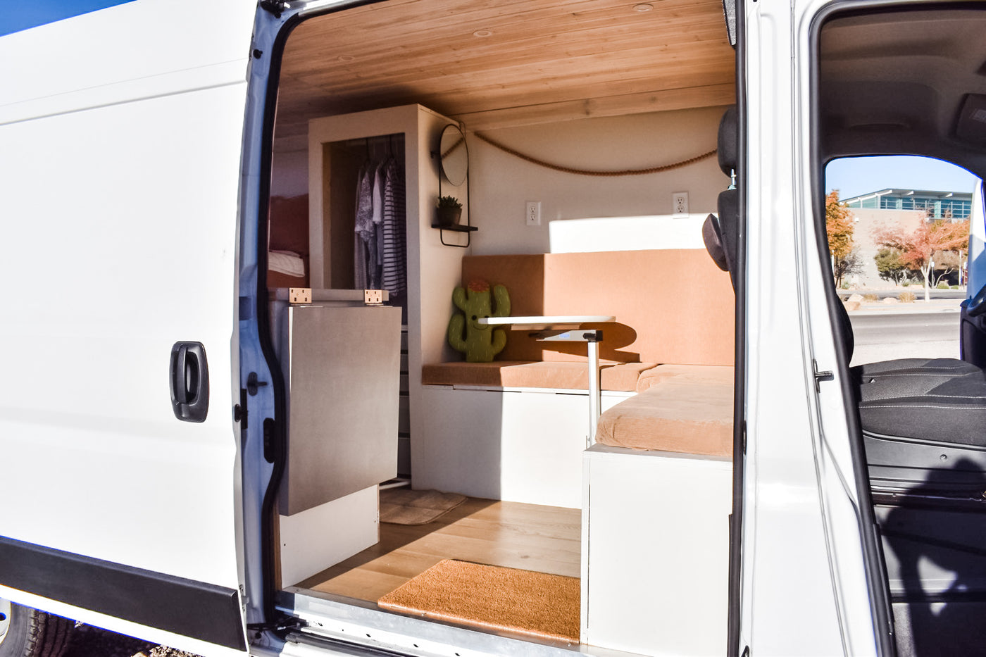 Inside an RV rental, a well-designed camper van interior with wood ceiling, seating, table, and storage. Open side door view. — photo 14