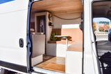 Inside an RV rental, a well-designed camper van interior with wood ceiling, seating, table, and storage. Open side door view.