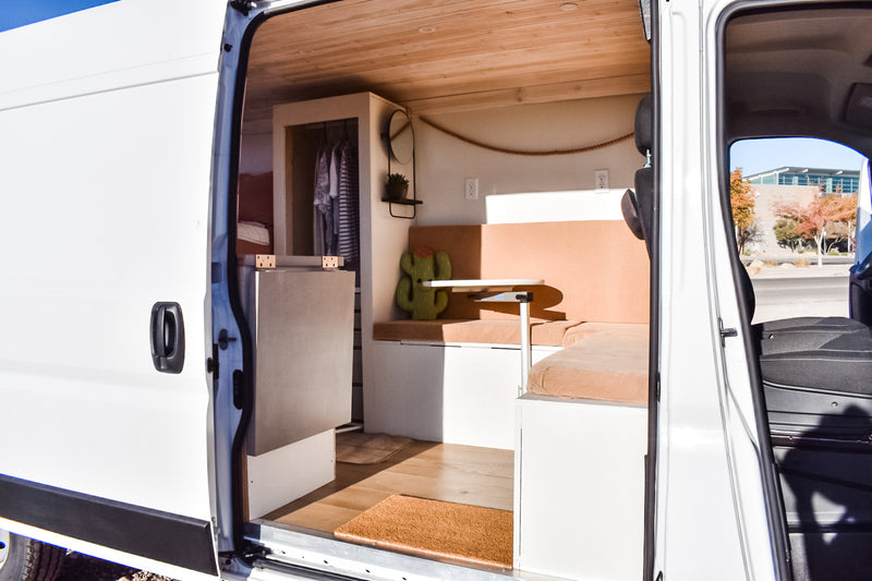 Inside an RV rental, a well-designed camper van interior with wood ceiling, seating, table, and storage. Open side door view. — photo 14
