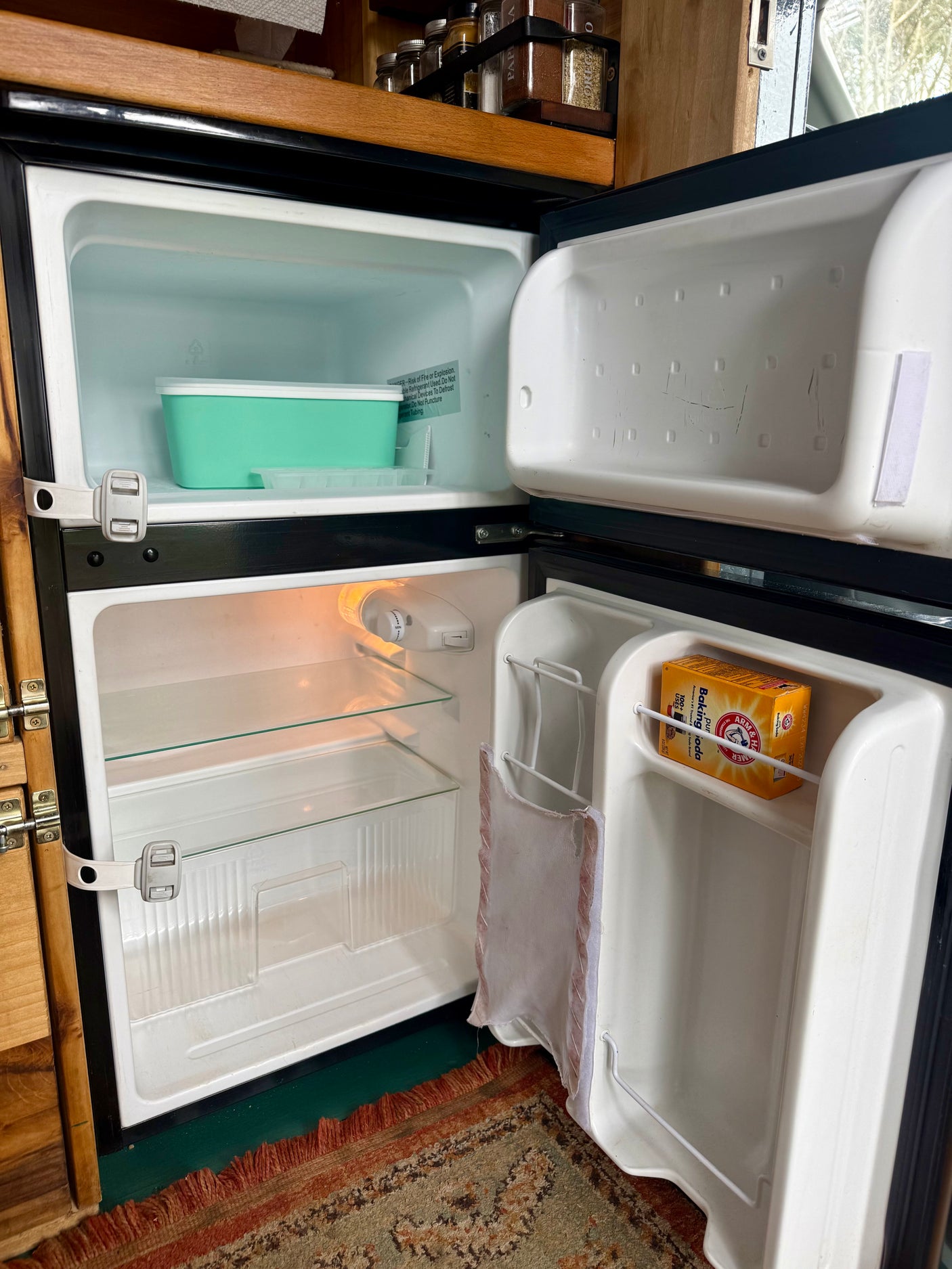 Inside an rv rental: open small refrigerator and freezer, showing baking soda on the door and latches for travel.