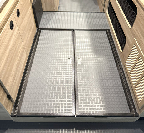 Detailed view of an RV rental's grey, non-slip floor with framed access hatches and pull tabs, flanked by wood paneling.
