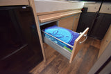 Practical RV rental interior featuring a partially open storage drawer with blue towels, next to a fridge and bed area.
