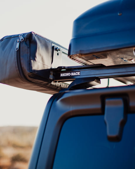 Detail of a Rhino-Rack rooftop system on an RV rental, featuring an awning case and cargo box. Perfect for outdoor travel.