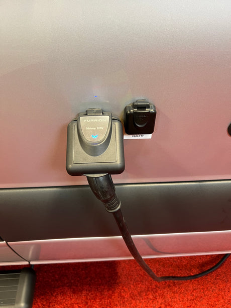Close-up of an RV rental's electrical hookup (Furrion 30A 125V) and Cable TV inlet, ready for use.