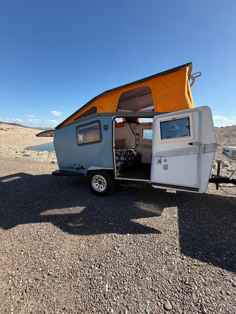 Sunny day by the lake with a light blue pop-top camper, an ideal rv rental for outdoor adventures and camping.