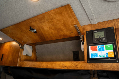 RV rental interior features: an open wooden cabinet and two digital displays for power monitoring and control.