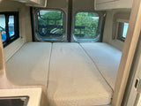 Inside a cozy rv rental: A modular bed with three segments, large windows, and a small sink area visible.