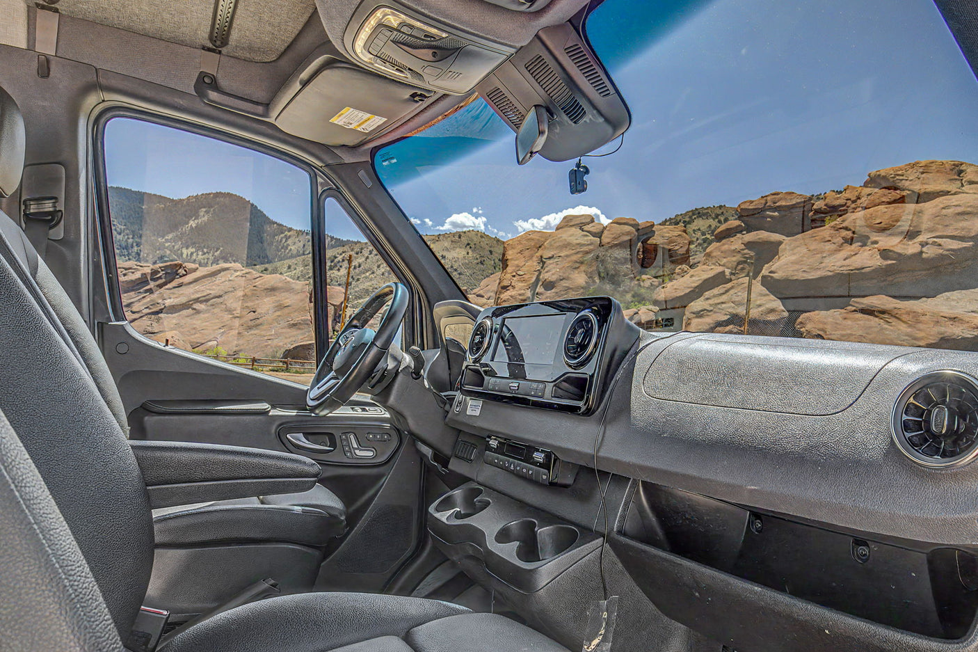 Modern rv rental van interior showing the dashboard, steering wheel, and a vast mountain vista outside under a blue sky.