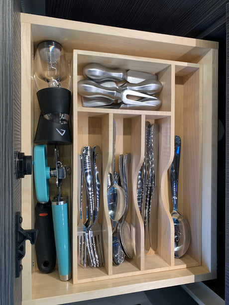 Organized RV rental drawer: compact cutlery, cheese tools, wine aerator, and can opener in a wooden organizer.