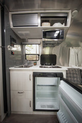 This rv rental's compact kitchen features a sink, stove, microwave, and open fridge with labeled overhead storage.