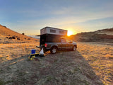 Truck camper RV rental set up for a golden hour outdoor adventure at sunset in a vast, dry landscape.