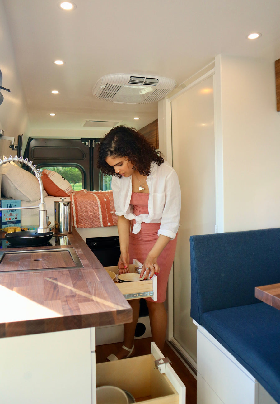 Woman utilizing smart kitchen storage in a modern RV rental, enjoying the comforts of mobile living.