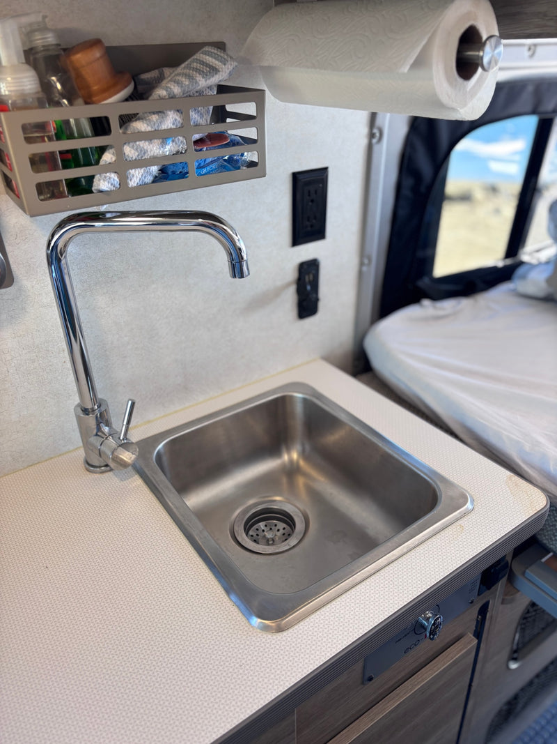 RV rental interior: Kitchenette with sink, faucet, paper towels, storage, and power outlets. Bed in background. — photo 18
