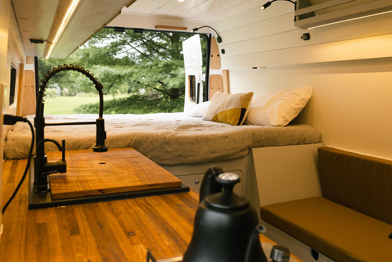 Modern RV rental interior with kitchen sink, comfy bed, and open back doors to nature, ideal for van life adventures. — photo 2