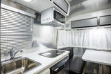 RV rental interior: A compact kitchen with sink, cooktop, microwave, and dining area, ideal for travel.