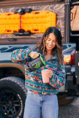 Smiling woman pouring from Jetboil into a cup, against an RV rental. Morning coffee for outdoor travel & camping adventures.