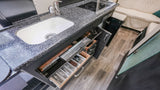Well-equipped RV rental kitchen interior: sink, induction cooktop, and open drawers reveal neatly organized utensils.