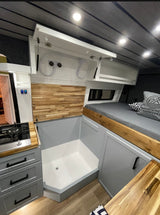 Modern RV rental interior with a compact wet bath, kitchen stove, and cozy bed. Ideal for van life comfort and travel.